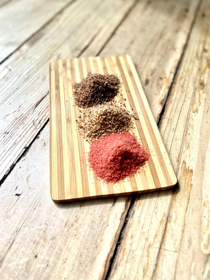 ChouAmi Gourmet Sea Salt Trio - three mounds of chipotle, hickory smoke, and alaea sea salt on a bamboo board.