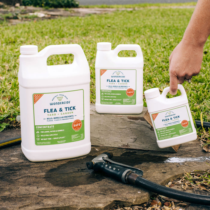 Three bottles of Wondercide Home Treatment Kit | Flea & Tick Spray are on green grass by a garden hose; one is held in hand. The scene features lush grass and a sidewalk, highlighting this effective home solution.