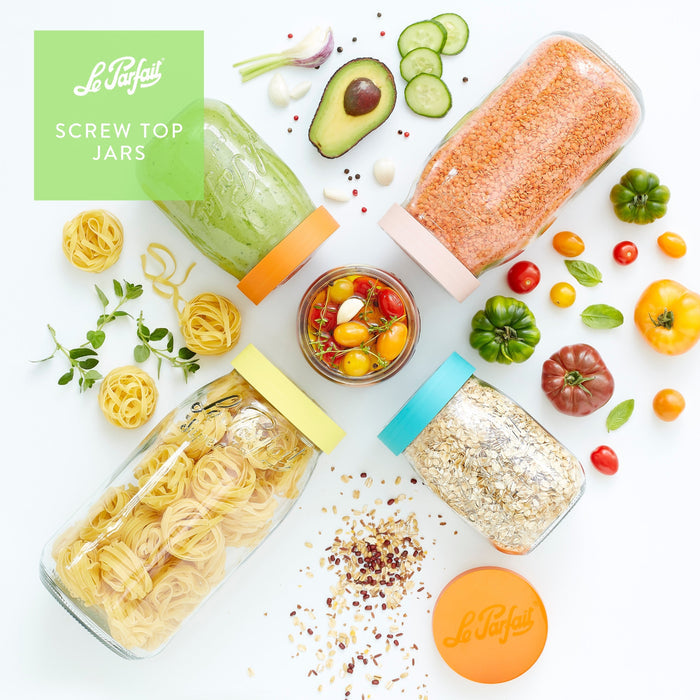 Top-down Le Parfait Screw Top Jars filled with green pesto, red lentils, tagliatelle, and oats among avocado, cucumber, tomatoes, and fresh herbs.