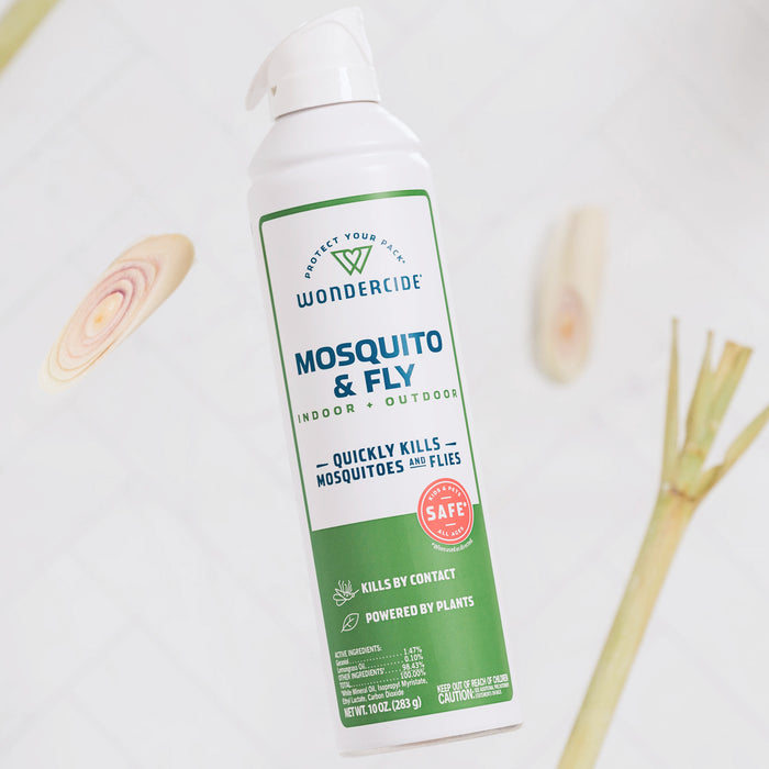 A can of Wondercide Mosquito & Fly for Indoor + Outdoor stands upright on a white surface with lemongrass pieces. The label shows it’s plant-powered, kills mosquitoes and flies, and is safe around pets.