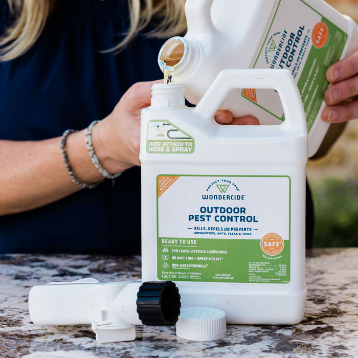 A person pours liquid into a white Wondercide Outdoor Pest Control Concentrate for Yard + Garden container with a detached sprayer and label visible on a marble surface.