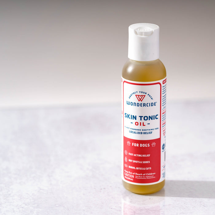 A bottle of Wondercide Skin Tonic Topical Oil for Dogs sits on a light surface, with a label highlighting fast-acting, localized relief for hot spots, sores, and bites—providing gentle care for dogs.